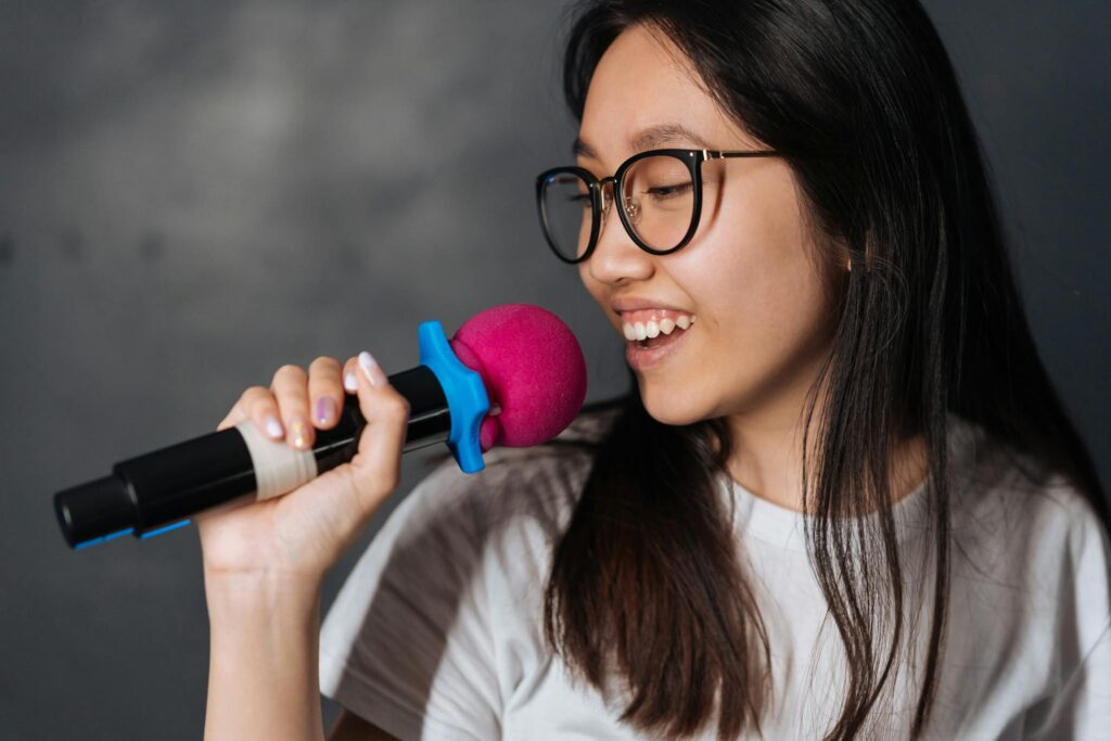 A young woman happily sings into a microphone during a karaoke session indoors.
