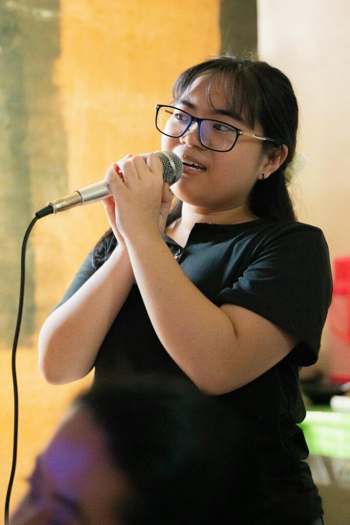 Young woman passionately singing karaoke with microphone indoors.